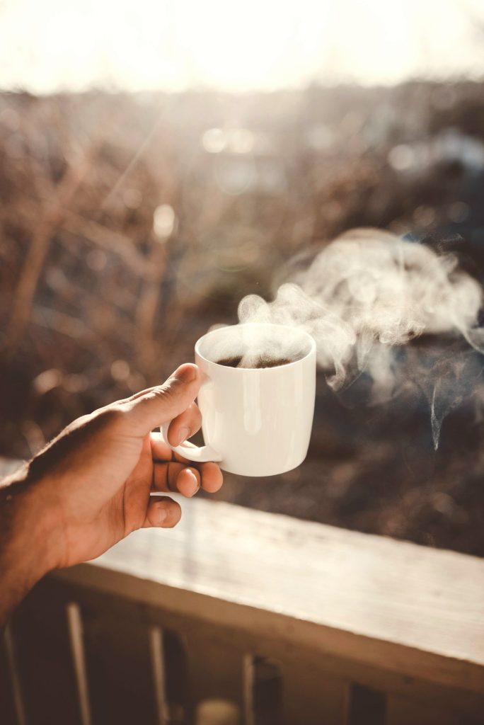 Hand holding a steaming cup of coffee in morning light